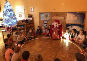 Dzieci siedzą w kole z Mikołajem.