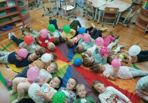 dzieci z balonami leżą na chuście animacyjnej.