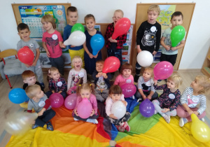 Dzieci z balonami siedzą na chuście animacyjnej.