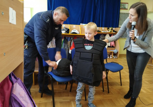 Policjant pomaga chłopcu założyć kamizelkę ochronną.