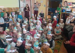 Dzieci z kolorowymi opaskami na głowach słuchają przedstawienia.