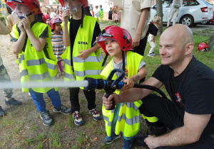 Chłopiec leje wodę z węża strażackiego.