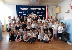Cała społeczność przedszkola pozuje do zdjęcia na tle dekoracji.