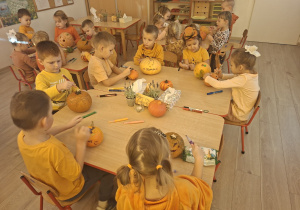 Dzieci z grupy I siedzą przy stoliczkach i ozdabiają dynie według własnego pomysłu.