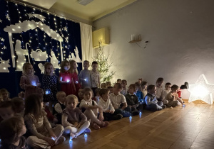 Dzieci trzymają w rączkach zapalone światełka i śpiewają kolędę.