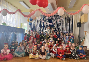 Zdjęcie wszystkich dzieci z przedszkola z Panią prowadzącą zabawę karnawałową. Na tle dekoracja.