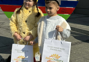 Chłopiec w przebraniu zajączka wielkanocnego i dziewczynka w przebraniu kurczaczka pozują do zdjęcia.