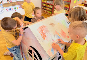 Dzieci współpracują podczas malowania papierowego przestrzennego domku.