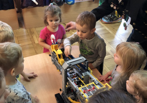 Dzieci oglądają model koparki wykonanej z klocków lego.