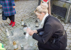 Nauczycielka zapala znicz pod pomnikiem.