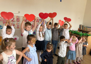Dzieci śpiewają i trzymają czerwone, papierowe serca.